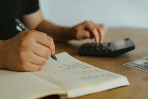 A man is seen writing his expenses in a notebook, emphasizing careful budgeting and financial tracking.