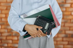 An individual grasping a calculator and a folder, engaged in a task that requires calculation and organization.