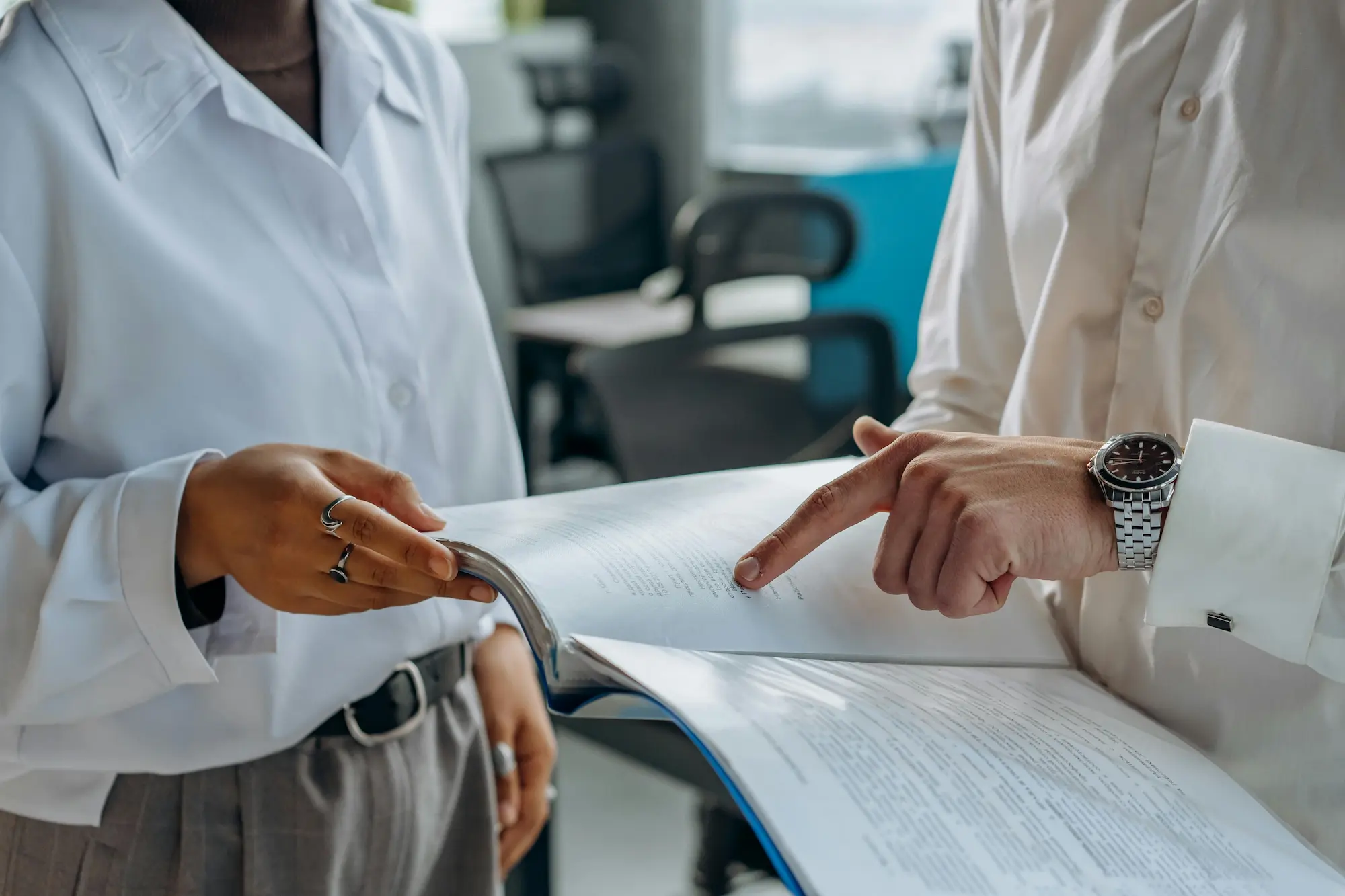 Two individuals dressed in business attire engaged in a conversation, each holding papers in their hands.