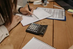 A focused woman takes notes in a notebook, accompanied by a calculator for her calculations.