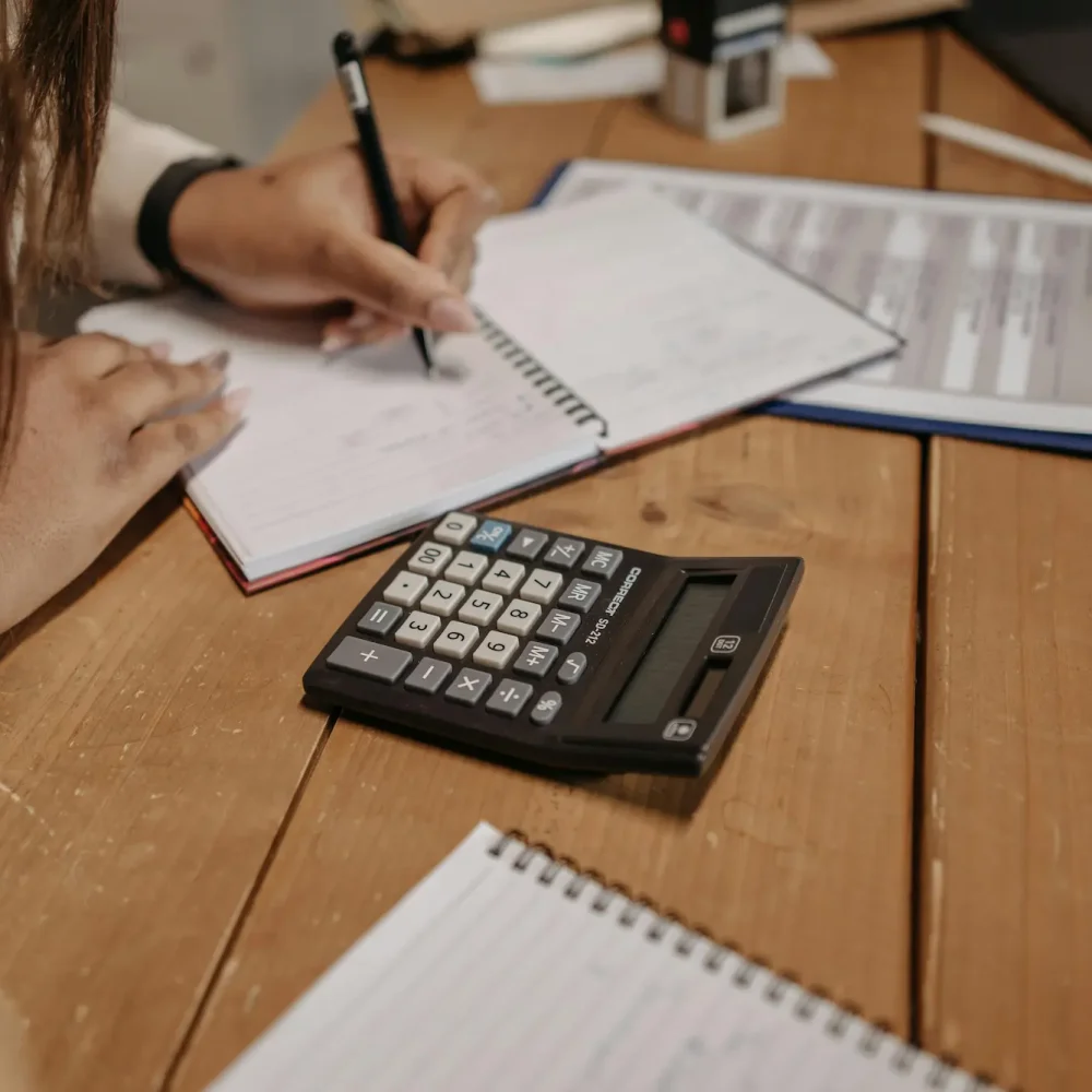 A focused woman takes notes in a notebook, accompanied by a calculator for her calculations.